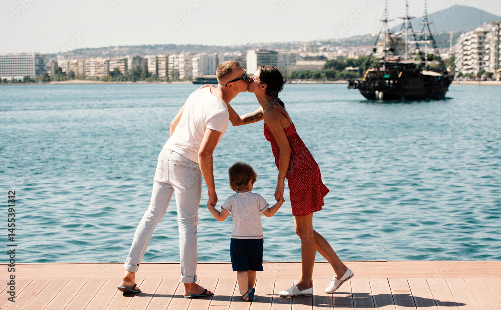 Young family enjoying summer by the sea. Father, mother, and child on summer vacation. Sea for happy family. Loving parents and child. Family summer vacation. Young family. Father kiss mother.