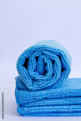 Vertical shot of rolled blue microfiber towel with low pile height on stack of towel isolated on white background