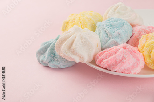 Pastel-colored marshmallows on white plate over pink background, sweet candy arrangement with soft colors and copy space
