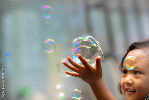 Cute Asian little girl happy playing soap bubbles outdoors in daylight