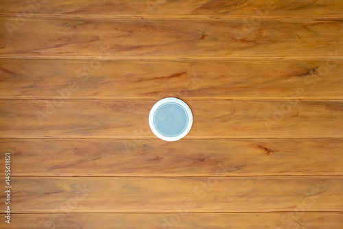 white circular ceiling speaker mounted on a warm-toned wooden plank ceiling with visible wood grain.