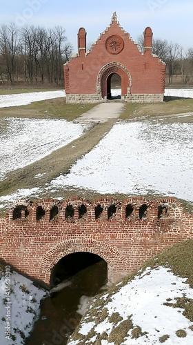 Red brick gateway and bridge in snowy parkland.  Historic architecture, winter landscape. Ideal for travel, history, or architecture websites