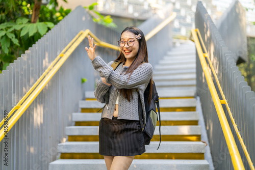 Wallpaper Mural Happy student greeting hello with friend, cheerful asian girl with backpack waving hand enjoying school life and fun learning at outdoors, showing positive energy and enthusiasm for education journey Torontodigital.ca