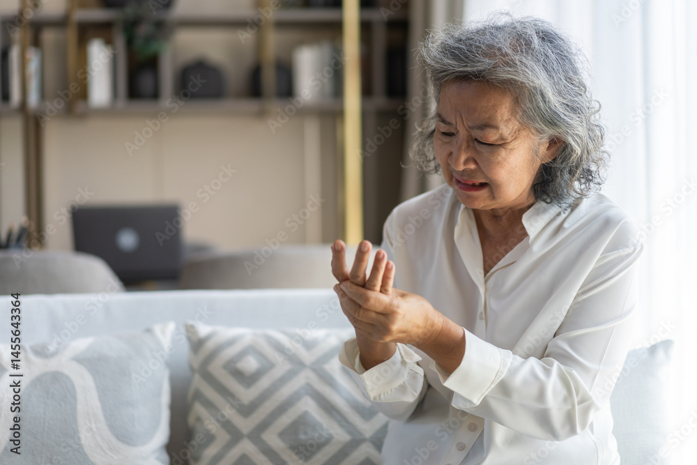© Art_Photo - Elderly asian woman holding wrist pain, arthritis, health issue, senior female suffering from joint pain at home, expressing discomfort, aging health problem, chronic condition indoor living room