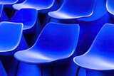 Rows of vibrant blue plastic chairs. Close-up view of many identical chairs,?arranged in a tight formation.?The color is a deep, saturated blue