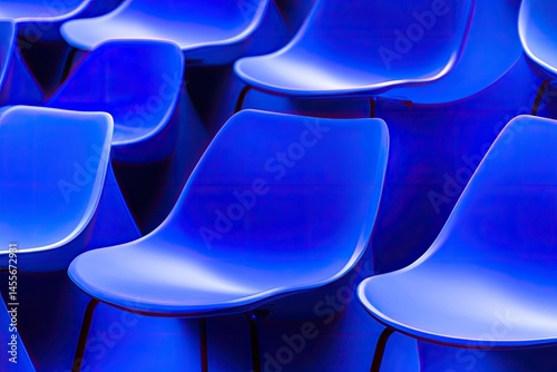 Rows of vibrant blue plastic chairs. Close-up view of many identical chairs,?arranged in a tight formation.?The color is a deep, saturated blue