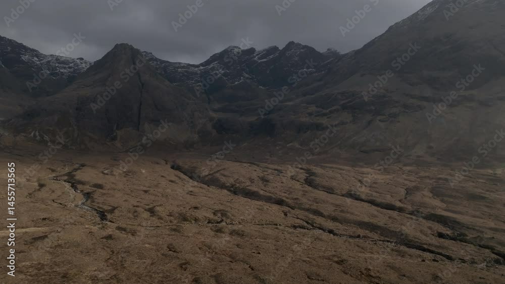 Aerial drone shot over the Fairy Pools valley on the Isle of Skye, lit by golden sunlight and framed by towering mountains with dramatic clouds drifting in the distance Aerial drone shot over the Fairy Pools valley on the Isle of Skye, lit by golden sunlight and framed by towering mountains with dramatic clouds drifting in the distance