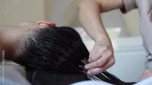 Close-up of a woman enjoying a Japanese head spa treatment, a relaxing scalp massage using a tool for hair and scalp care at a beauty salon. Focus on the soothing, calming process of hair therapy	
