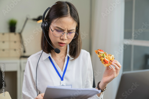 Asian businesswoman eating pizza while working with clients due to rush hour.