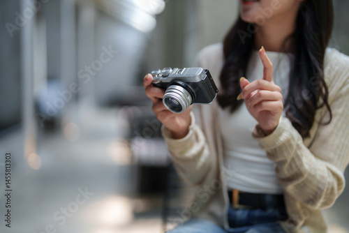 Photographer is showing how to use professional compact mirrorless camera explaining something with her finger while holding a camera in her hands