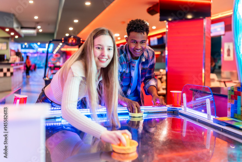 Young multiethnic friends playing air hockey in entertainment center