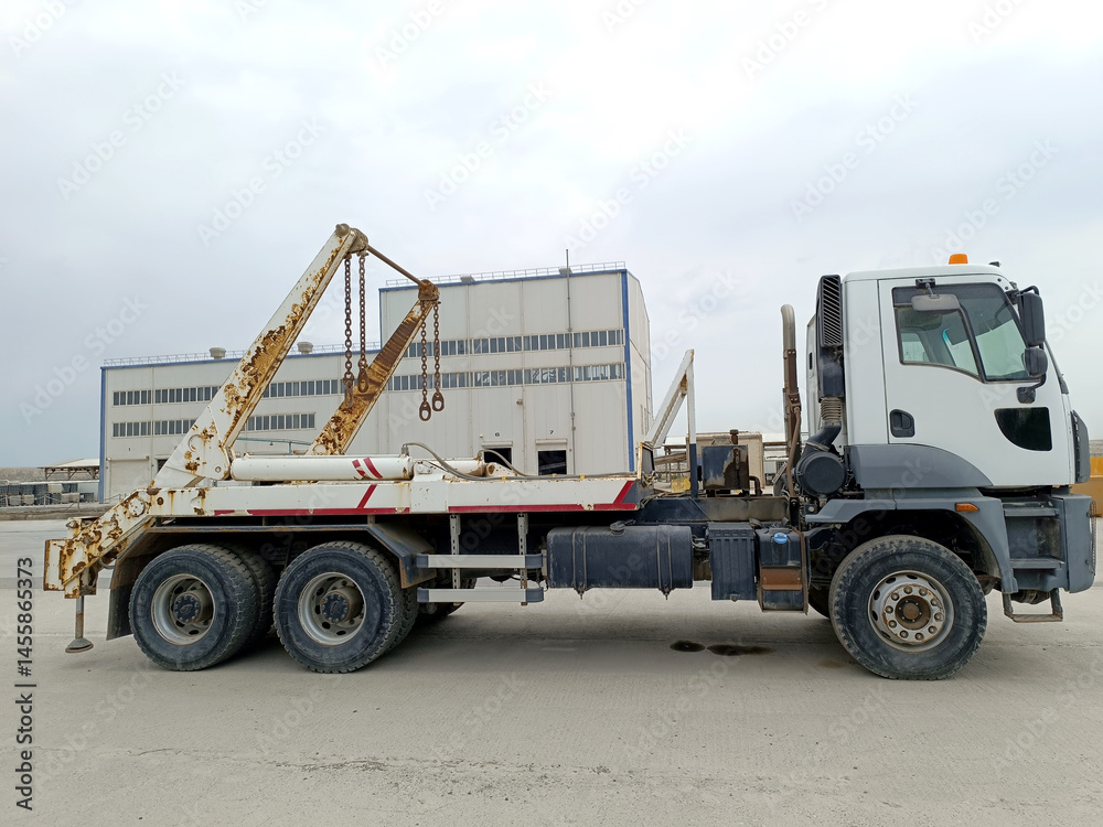 Skip loader on the factory premises. Skip truck surrounded by containers and factory in the open air Skip loader on the factory premises. Skip truck surrounded by containers and factory in the open air