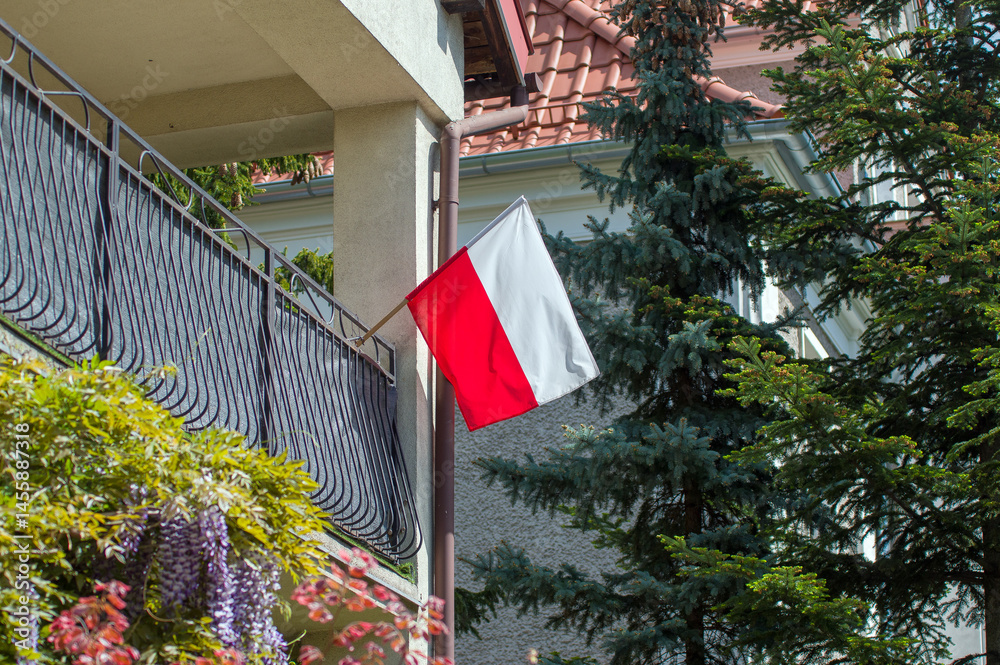 Biało czerwona flaga Polski umocowana na balustradzie balkonu.