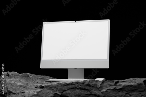 Sleek monitor and keyboard on a rocky surface.