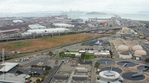 Aerial pullback shot of water wastewater treatment plan in Oakland and shipping harbor with cargoes and San Francisco skyline