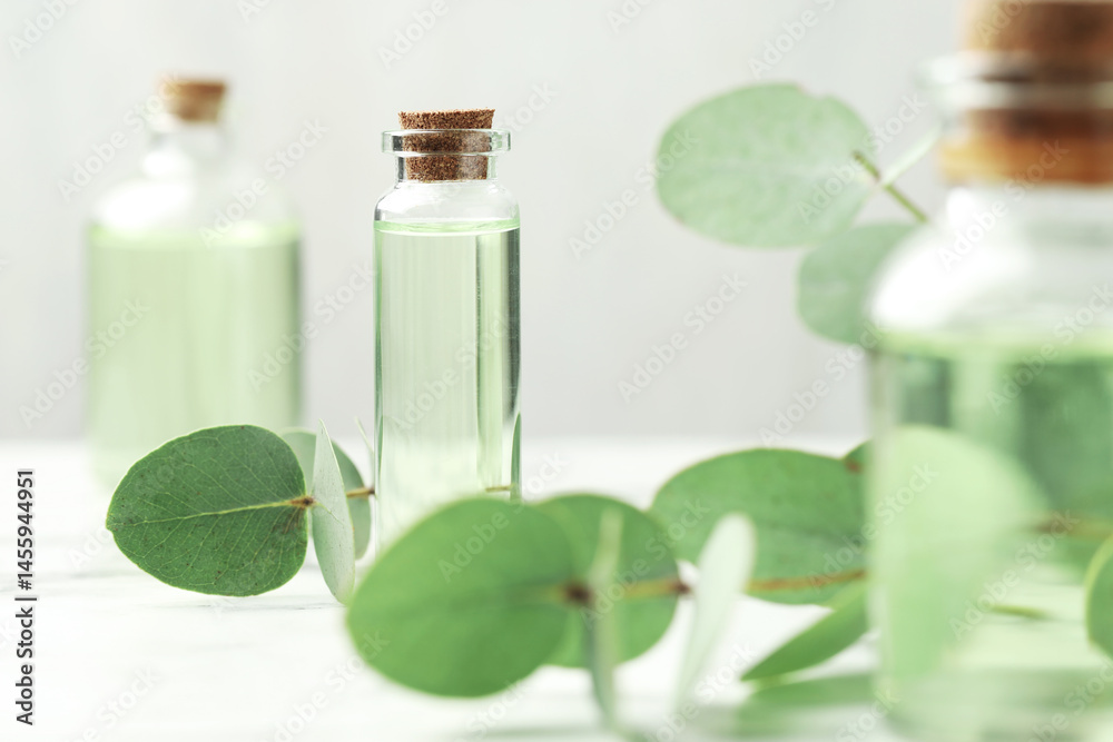 Bottles of essential oil and eucalyptus leaves on white table, closeup Bottles of essential oil and eucalyptus leaves on white table, closeup