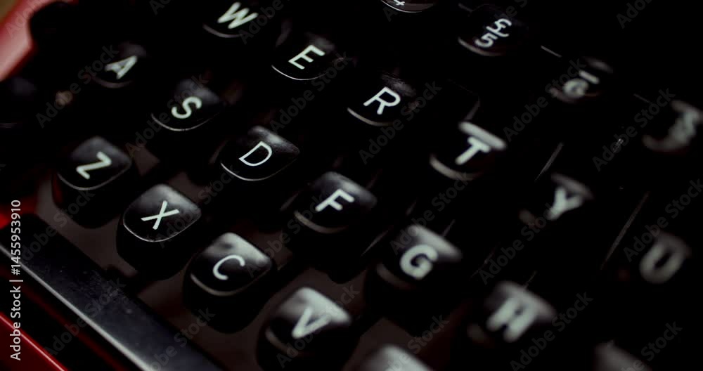 Close-up of a black vintage typewriter keyboard with white QWERTY keys. Slightly blurred lower keys create depth, red trim accents, wooden background. Elevated angle.