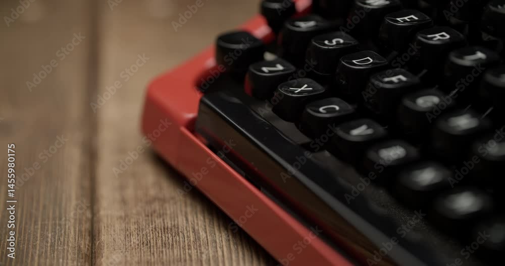 Close-up of a black vintage typewriter keyboard with white QWERTY keys. Slightly blurred lower keys create depth, red trim accents, wooden background. Elevated angle.
