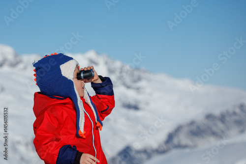 Obraz na płótnie Young kid boy in blue funny hat views snowy peaks at binocular w salonie