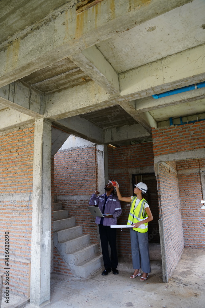 Black male engineer as foreman and Latin female construction inspector wearing construction helmet standing holding walkie talkie talking and consulting on construction of house project