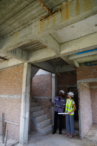 Obraz na płótnie Black male engineer as foreman and Latin female construction inspector wearing construction helmet standing holding walkie talkie talking and consulting on construction of house project w salonie