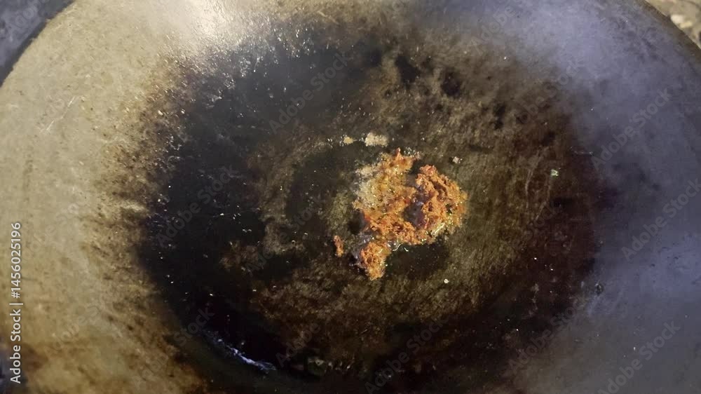 Asian cook is cooking in thai kitchen in local traditional country style, preparing sizzling thai green curry paste being stir fried in traditional wok to cook thai food green curry popular worldwide