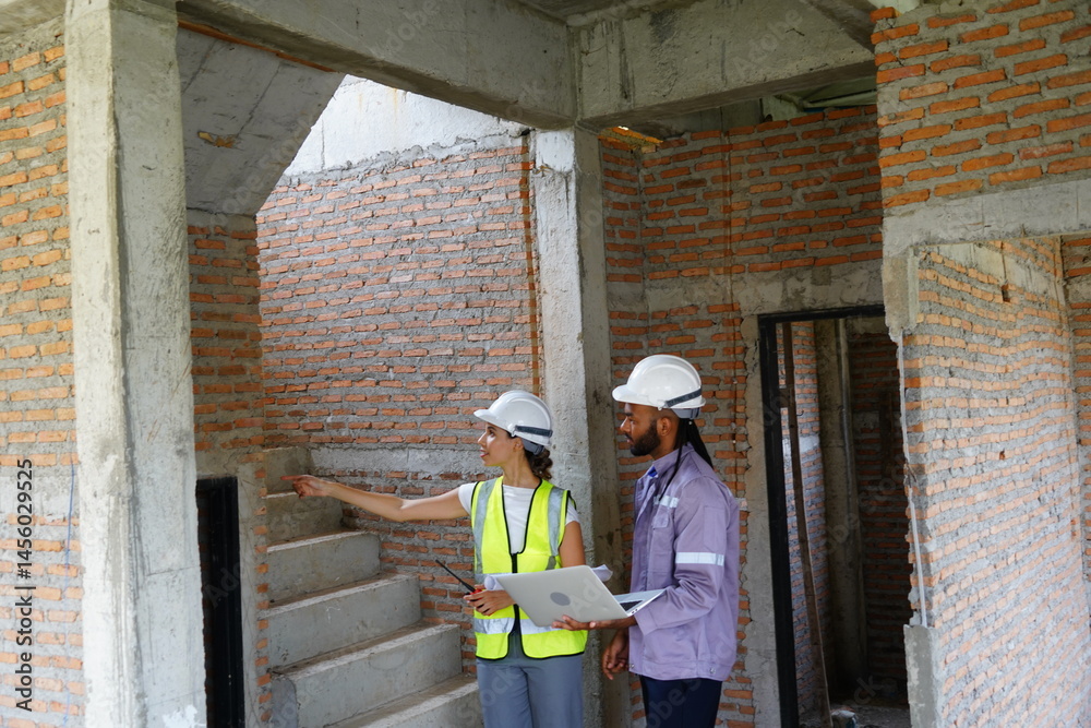Black male engineer as foreman and Latin female construction inspector wearing construction helmet standing holding walkie talkie talking and consulting on construction of house project