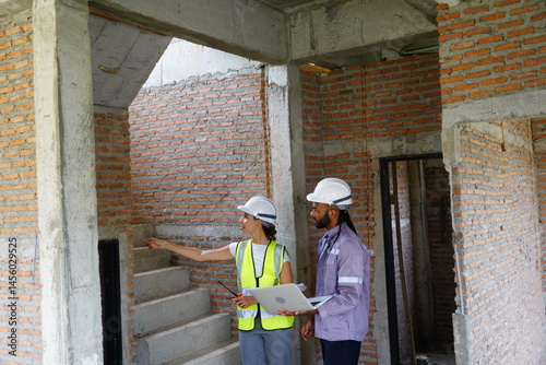 Obraz na płótnie Black male engineer as foreman and Latin female construction inspector wearing construction helmet standing holding walkie talkie talking and consulting on construction of house project w salonie