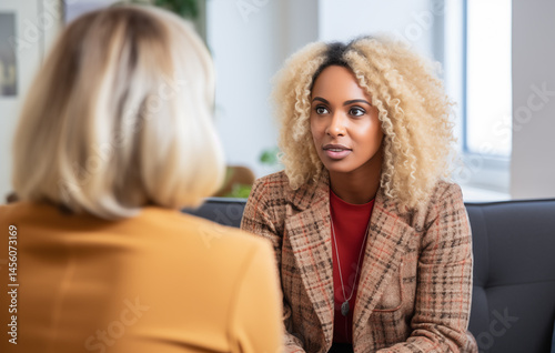 In a well-lit office, a woman with curly hair listens intently to another woman with straight hair. Both seem engaged in a meaningful discussion, showcasing a moment of connection