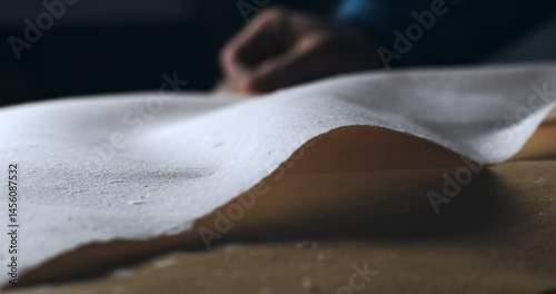 Super Slow Motion Macro of Handmade Paper Sheet Being Carefully Handled on a Wooden Surface, Showcasing Its Texture, Deckled Edges, and Natural Imperfections in a Craft or Artistic Studio Environment.