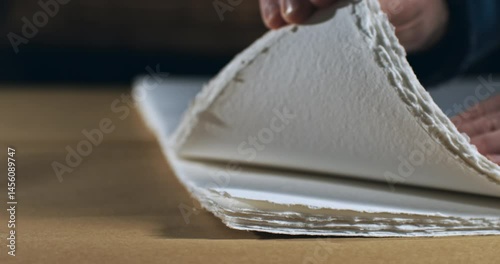 Super Slow Motion Close-Up of Hands Gently Lifting Deckle-Edged Handmade Cotton Paper Sheets on Wooden Table in Artisan Studio, Emphasizing Texture, Craftsmanship and Fine Art Materials at 1000 fps.