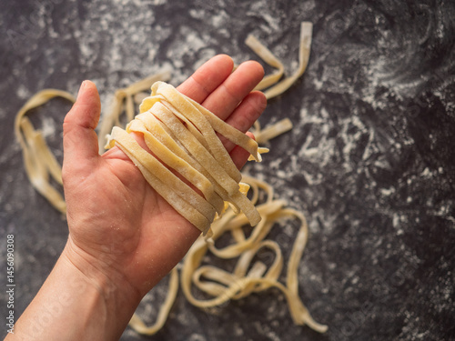 Holding a bunch of pasta over a dark kitchen counter with more pasta in the background. 