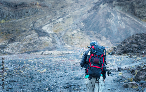 Backpacker hiking on volcanic loose scree at Tongariro Alpine crossing, Unrecognizable hikers in the distance. Tongariro National Park. New Zealand.