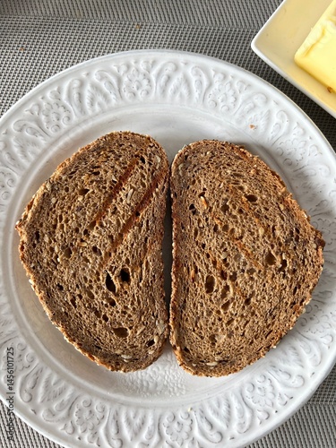 Dos rebanadas de pan de molde integral de Centeno tostadas, colocadas en un plato blanco para el desayuno, de forma simétrica vertical, vistas desde arriba