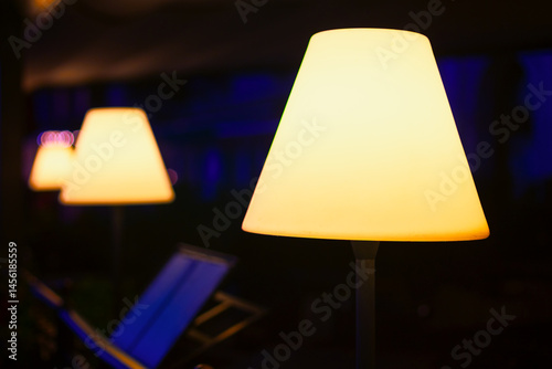 Obraz na płótnie Row of illuminated lamps with conical shades, creating a warm and inviting atmosphere. Background is dark with a hint of blue light, making the glowing lamps stand out prominently w salonie
