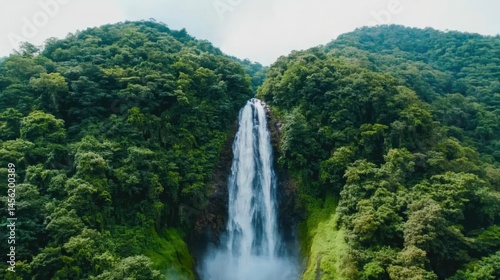 Majestic waterfall cascading through lush green mountains in a tropical rainforest setting under a clear sky