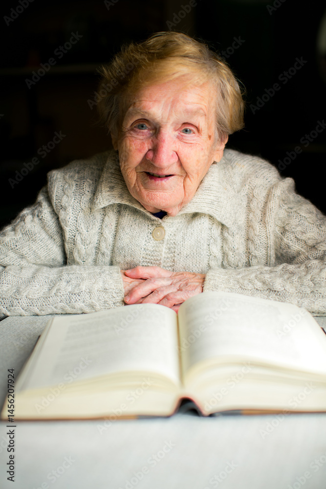 An elderly woman sits at a table reading a thick book, immersed in quiet concentration and surrounded by a sense of wisdom and calm.