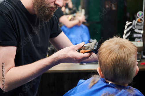 Hairdresser using electric shaver to cut boy's hair. Little kid getting first haircut in barbershop. Close up