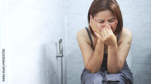 asian woman sitting on the toilet and experiencing foul-smelling stools and diarrhea, possibly caused by digestive issues such as inflammatory bowel disease, infections, food intolerances, or allergie