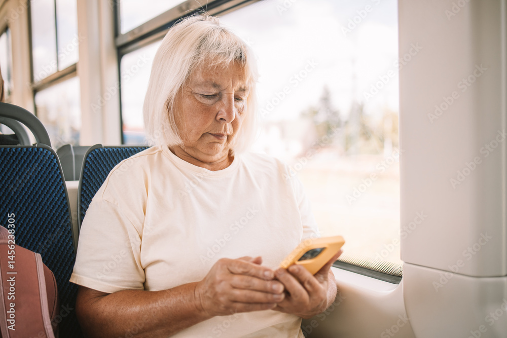 A senior woman wearing a pink hat is sitting on a bus, using her smartphone. She is traveling through the city, enjoying her journey in a relaxed manner.