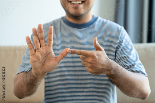Portrait view of happy young deaf asian man showing sign language and looking at camera at home, a man with hearing disability having communication with hands gestures concept.