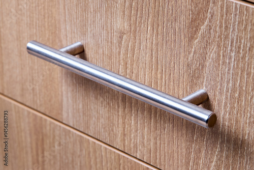 Rectangle shaped kitchen cabinet with stainless steel brushed handles close up selective focus shot. Cabinet door adorned with metal handles