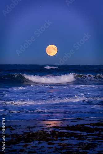 Full moon over a dark ocean. Waves crash on the shore.