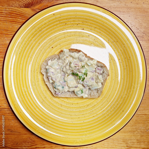 Obraz na płótnie A slice of bread topped with an egg salad mixed with ham and spring onions is presented on a yellow plate on a wooden surface w salonie