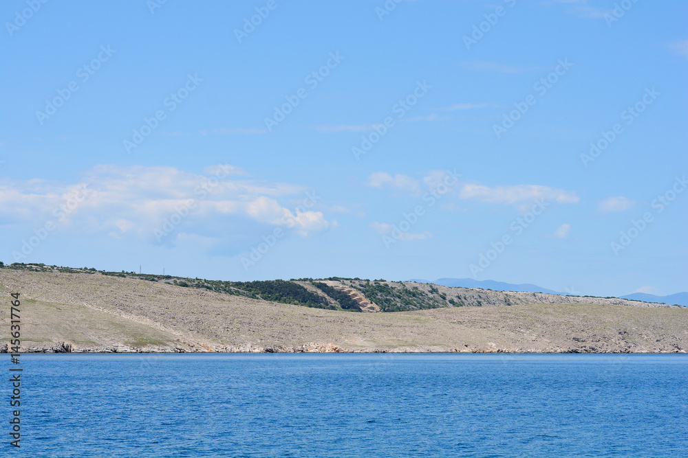 A serene view from Jadranovo shows the rugged coastline of Krk Island meeting the calm blue waters under a partly cloudy sky
