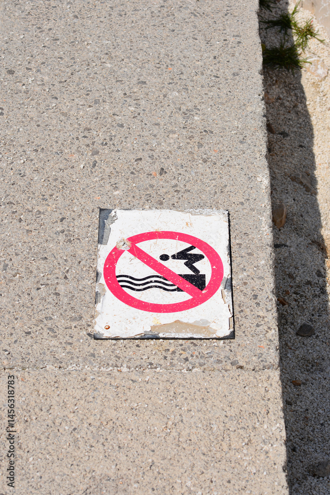 A weathered - No Diving - sign with a red circle and diagonal line over a diving figure is embedded in a concrete surface