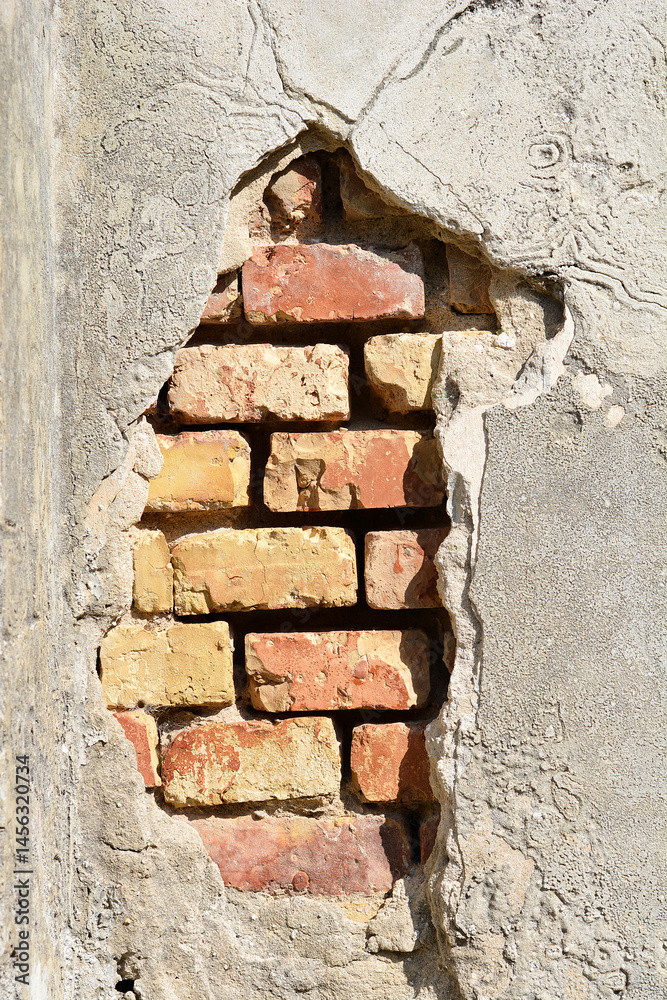 A section of a weathered wall shows exposed red and yellow bricks beneath crumbling gray plaster