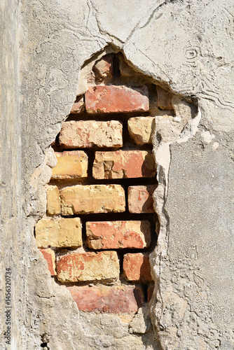 Obraz na płótnie A section of a weathered wall shows exposed red and yellow bricks beneath crumbling gray plaster w salonie
