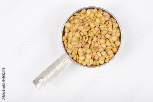 A top-down close-up shows a stainless steel measuring cup filled with plump, light brown rehydrated raw lentils against a plain white background