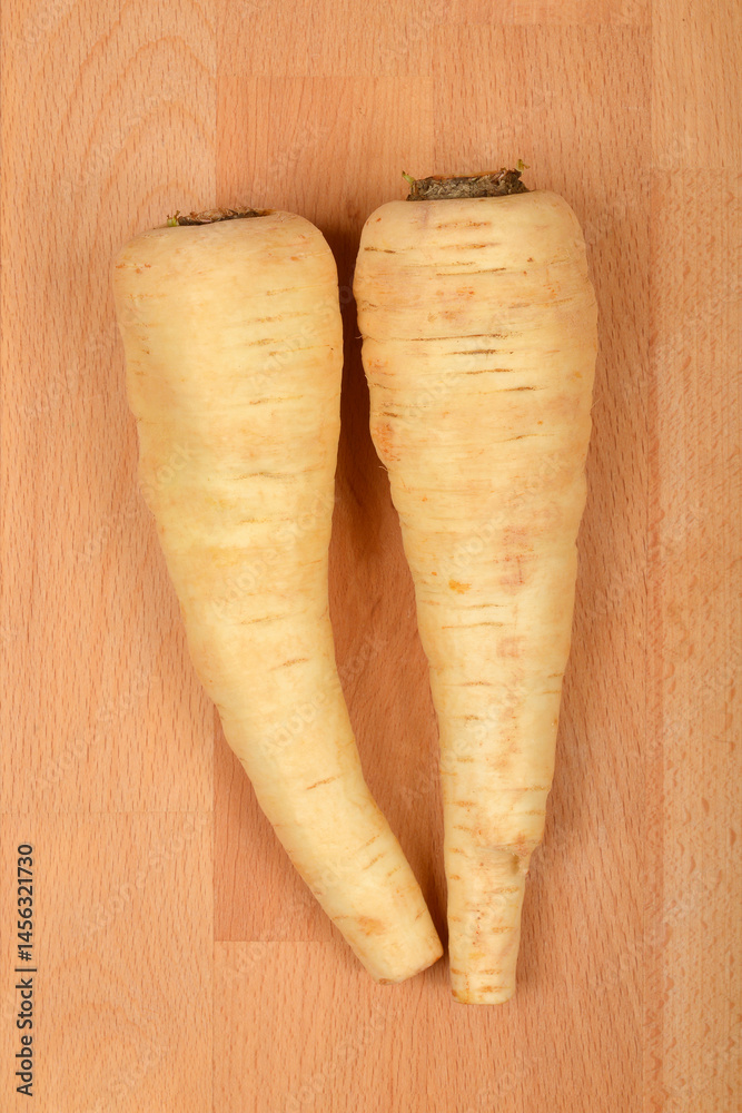 Two beige parsnips are positioned parallel on a light brown wooden surface